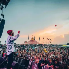 Bühnenkünstler wirft roten Ball in die Menge beim Watt en Schlick Festival Dangast. Ein Meer aus Menschen feiert unter dem Abendhimmel.