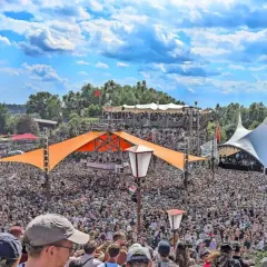 Tausende feiern auf dem Fusion Festival Ort unter blauem Himmel. Bunte Zelte und Bühnen prägen die Szenerie.