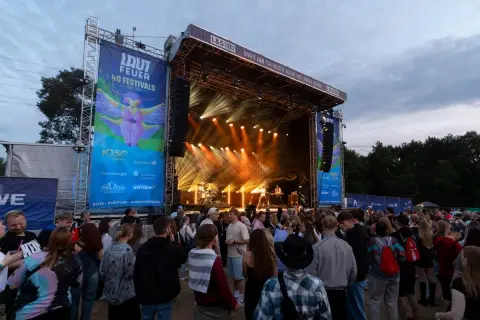 Menschenmenge vor einer Bühne beim lautfeuer festival. Scheinwerfer beleuchten die Bühne, auf der Musiker spielen.