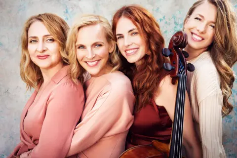 Vier lächelnde Frauen, eine davon hält ein Cello. Salut salon mitglieder, bereit für den Auftritt.
