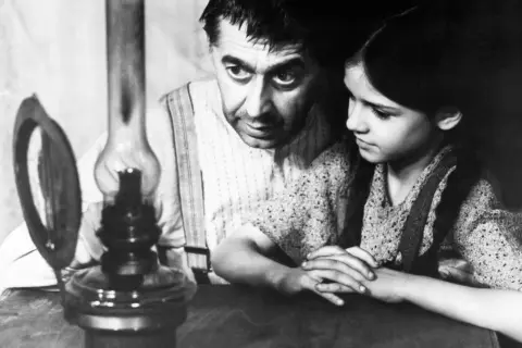 Ein Mann und ein Mädchen beugen sich über eine Öllampe. Ein Ausschnitt aus einem DDR-Film, vielleicht in der Mediathek zu finden.