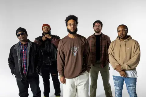 Fünf Männer stehen vor weißem Hintergrund. Einer trägt ein **butcher brown** Langarmshirt mit einem Hirschgeweih-Symbol.