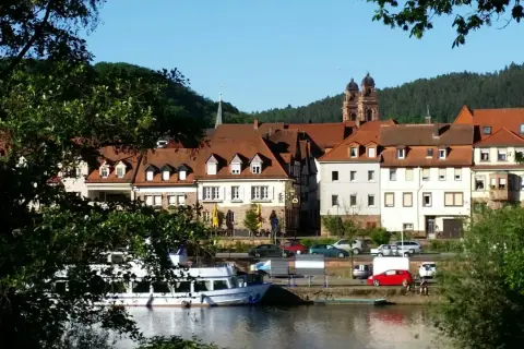 Idyllische Kulisse am Flussufer mit Fachwerkhäusern und Kirchturm. Vielleicht gibt es heute Veranstaltungen in Mosbach?