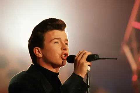 Junger Rick Astley singt mit Leidenschaft ins Mikrofon, sein ikonischer Look ist bereits erkennbar.