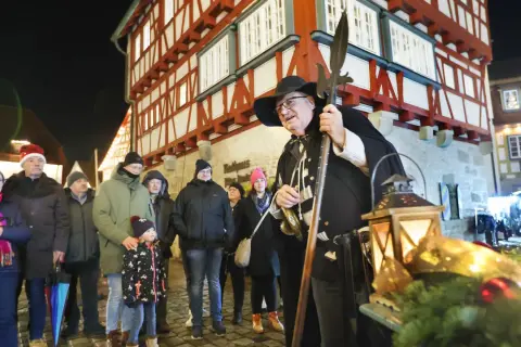Ein Nachtwächter mit Hellebarde und Laternen auf dem Vellberg Weihnachtsmarkt. Besucher in Weihnachtsmützen und warmen Jacken stehen davor.