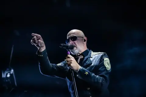 Der Sänger von Eisbrecher Ludwigsburg, mit Sonnenbrille und markanter Jacke, singt ins Mikrofon und zeigt mit dem Finger ins Publikum.
