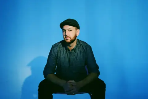 Matt Simons, nach dem Erdrutsch, sitzt nachdenklich vor blauem Hintergrund.