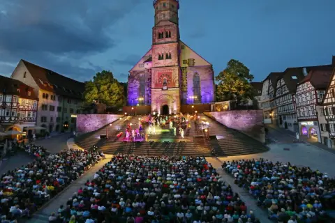 Bühnenaufführung vor historischer Kulisse in Hohenlohe. Ein großes Publikum verfolgt gespannt die Darbietung auf illuminierten Treppen vor einer Kirche.