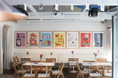 Bunte Bilder zieren die Wand im theater la lune Stuttgart. Kleine Tische mit Blumen laden zum Verweilen ein.