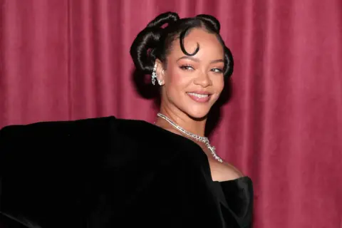 Rihanna lächelt in die Kamera, ihr Haar ist zu zwei eleganten Knoten hochgesteckt. Man fragt sich, ob sie bald ein neues Lied veröffentlicht.