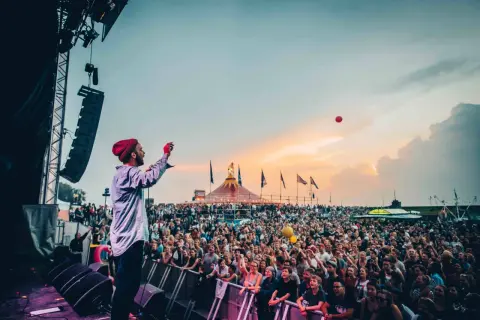 Bühnenkünstler wirft roten Ball in die Menge beim Watt en Schlick Festival Dangast. Ein Meer aus Menschen feiert unter dem Abendhimmel.