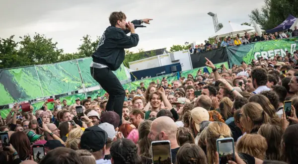 Sänger auf dem Dach eines Containers beim Green Juice Festival, der ins jubelnde Publikum zeigt. Viele Handys halten die Momente fest.