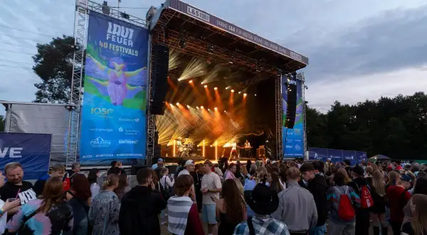 Menschenmenge vor einer Bühne beim lautfeuer festival. Scheinwerfer beleuchten die Bühne, auf der Musiker spielen.