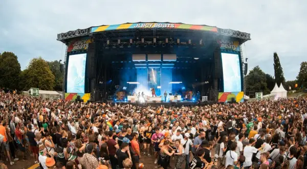 Riesige Menschenmenge feiert bei Juicy Beats 2025. Eine Bühne mit Lichtern und Bildschirmen, auf denen "Juicy Beats" steht, ist im Hintergrund zu sehen.
