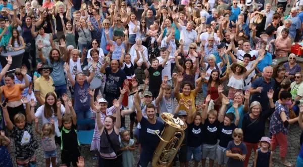 Große Menschenmenge winkt fröhlich bei Brackenheim Veranstaltungen. Ein Mann hält eine Tuba, Kinder und Erwachsene sind begeistert.