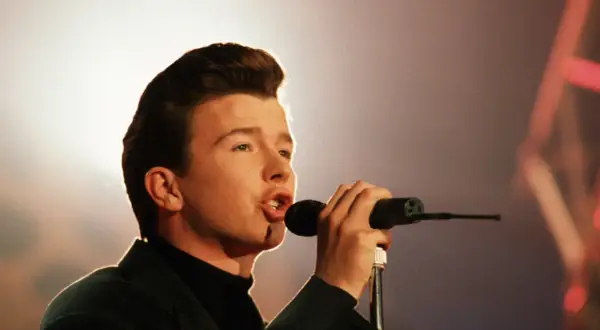 Junger Rick Astley singt mit Leidenschaft ins Mikrofon, sein ikonischer Look ist bereits erkennbar.