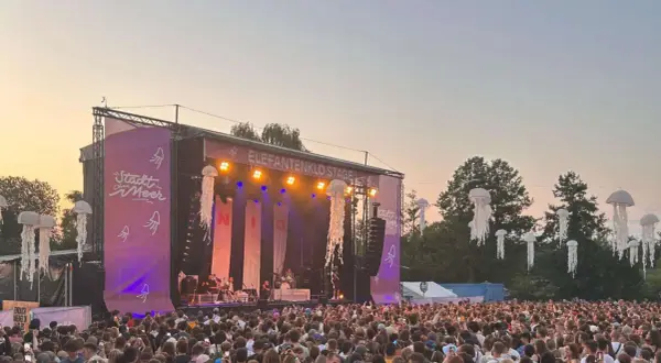 Große Menschenmenge feiert beim Stadt ohne Meer Festival. Die Elefantenklo Stage ist beleuchtet, Quallen-Deko schwebt in der Luft.