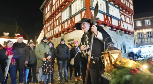 Ein Nachtwächter mit Hellebarde und Laternen auf dem Vellberg Weihnachtsmarkt. Besucher in Weihnachtsmützen und warmen Jacken stehen davor.