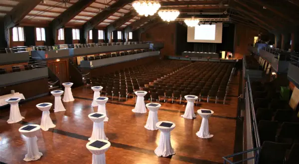 Innenansicht der Stadthalle Herrenberg mit vielen Sitzreihen, einer Bühne und Stehtischen, bereit für eine Veranstaltung.