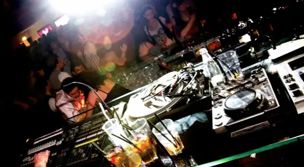 DJ-Pult mit Drinks und tanzenden Menschen im Hintergrund. Ein typischer Abend im **lifestyle club**.