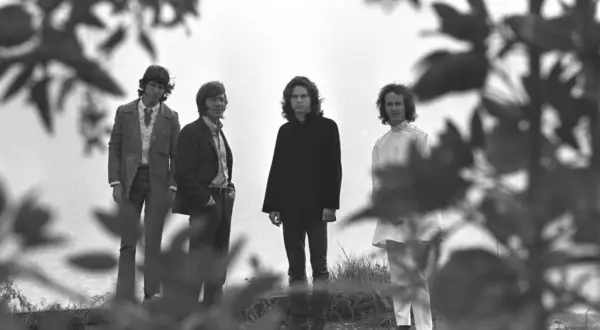 Die Mitglieder von The Doors stehen in einer Reihe, umgeben von Ästen und Blättern.