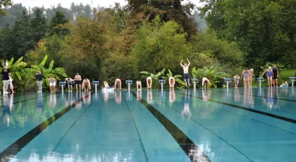 Menschen starten einen Wettkampf im untergruppenbach freibad. Einige springen von den Startblöcken, andere warten.
