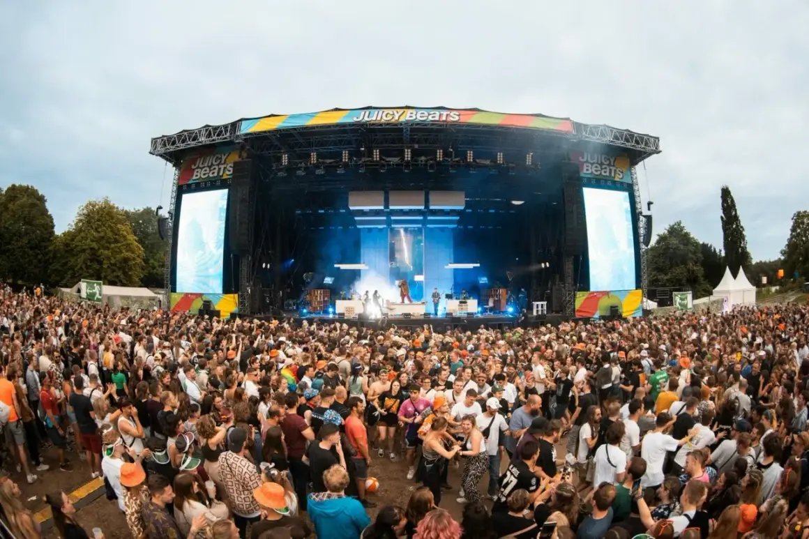 Riesige Menschenmenge feiert bei Juicy Beats 2025. Eine Bühne mit Lichtern und Bildschirmen, auf denen "Juicy Beats" steht, ist im Hintergrund zu sehen.
