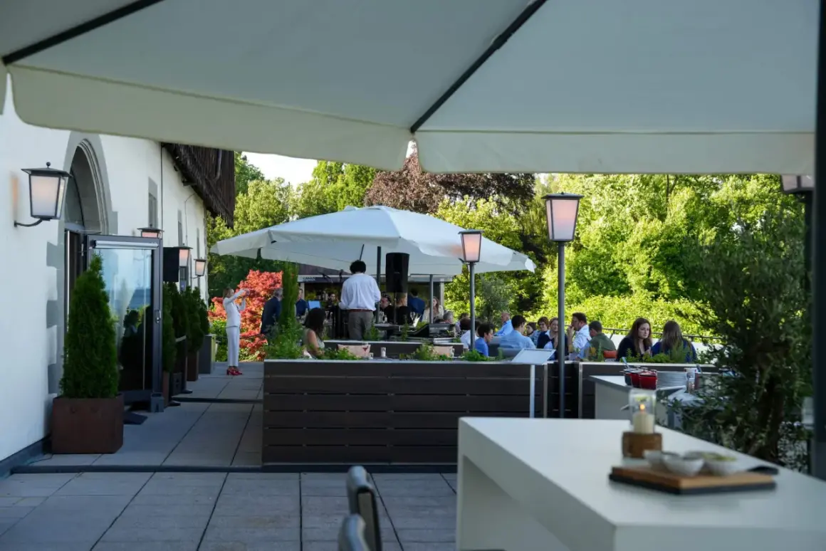 Gäste genießen den Abend im **Haigern Restaurant** auf der Terrasse unter Sonnenschirmen, mit grünen Bäumen im Hintergrund.