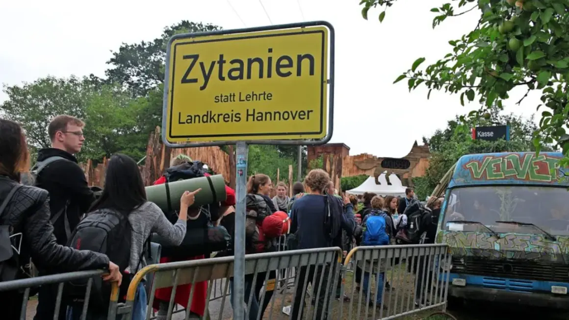 Besucher stehen vor einem Schild "Zytanien statt Lehrte, Landkreis Hannover". Ein bunt bemalter Van und Festivalbauten sind im Hintergrund zu sehen.
