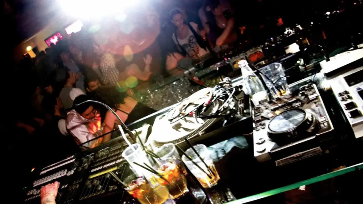 DJ-Pult mit Drinks und tanzenden Menschen im Hintergrund. Ein typischer Abend im **lifestyle club**.