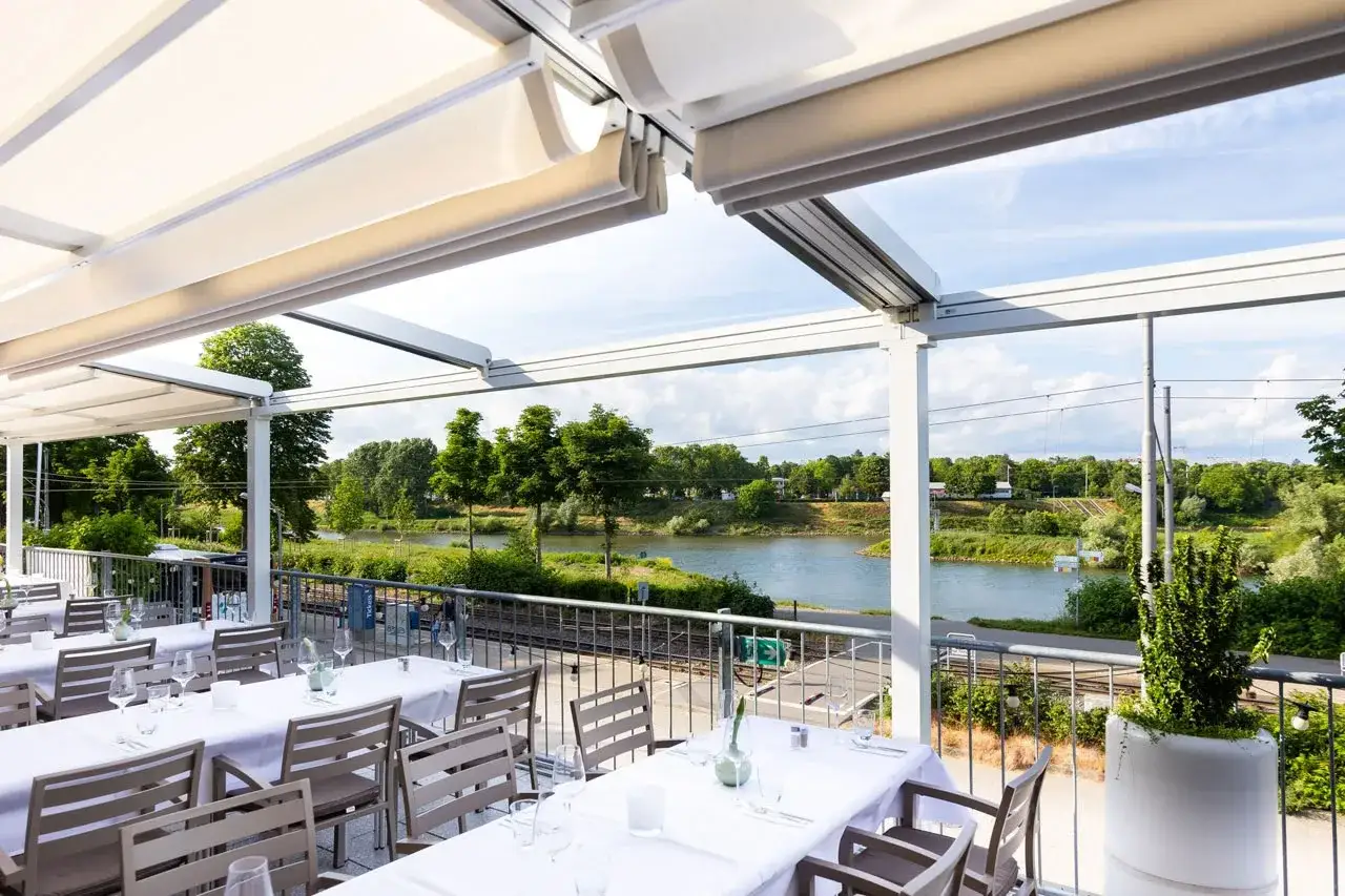 Terrasse des Bootshaus Neckarsulm mit Blick auf den Neckar. Gedeckte Tische laden zum Verweilen ein.